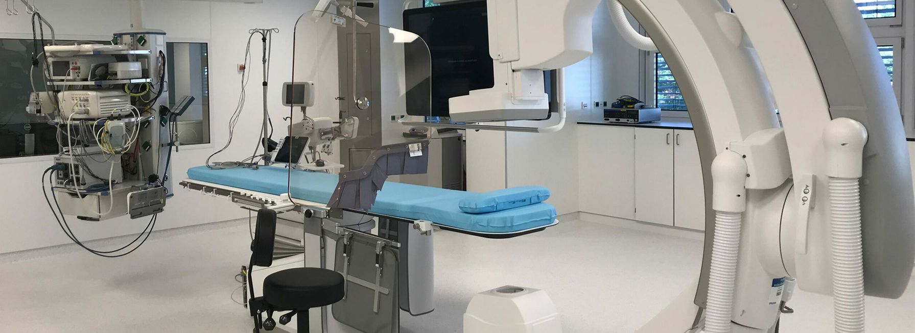 Ein moderner Untersuchungsraum verfügt über fortschrittliche Bildgebungsgeräte, einen verstellbaren Untersuchungstisch mit blauer Polsterung und eine sterile Umgebung.