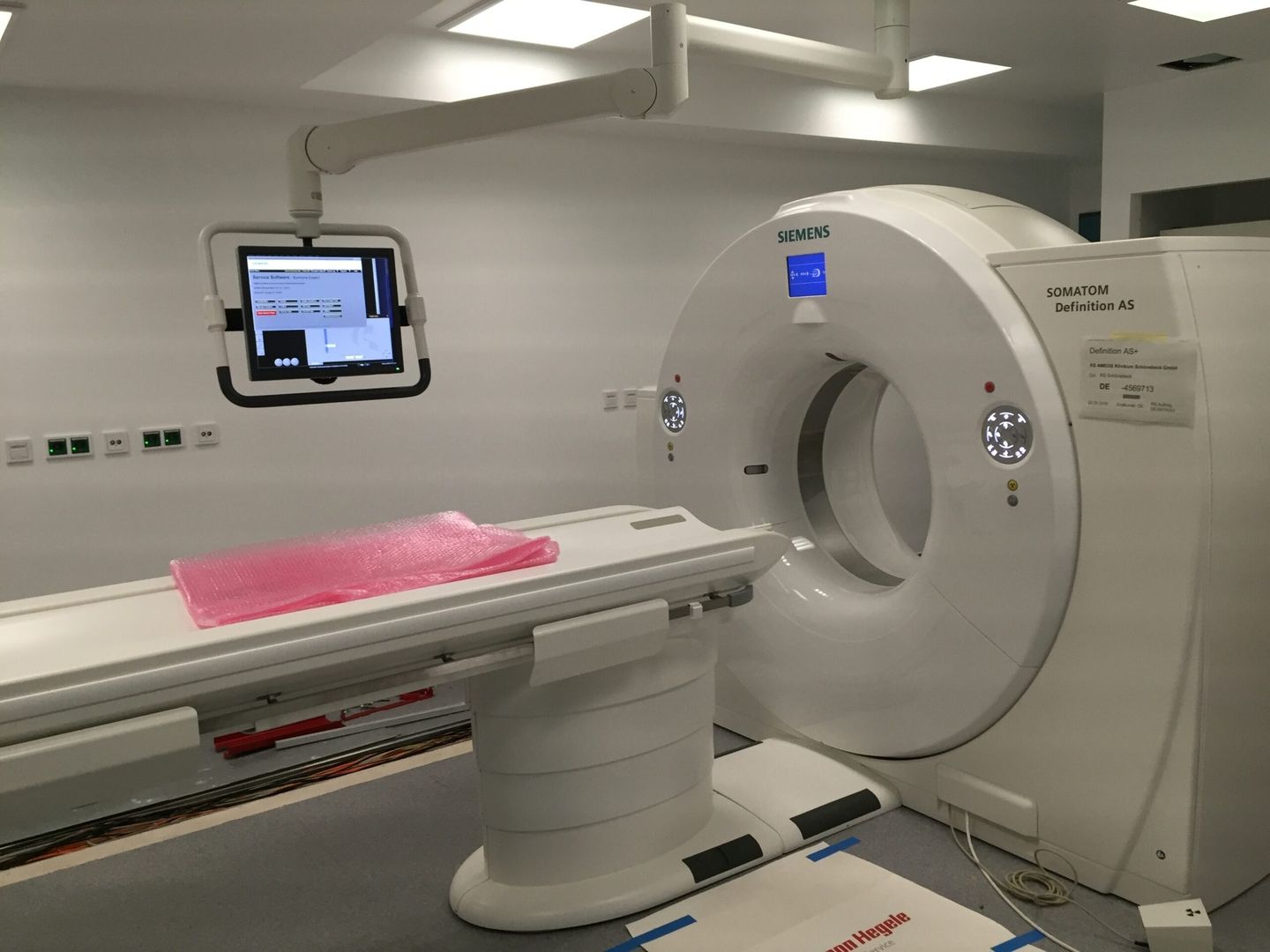 Ein Siemens SOMATOM Definition AS CT-Scanner mit einem Monitor über dem Patiententisch, der die Einstellungen in einem sauberen, gut beleuchteten Raum anzeigt.