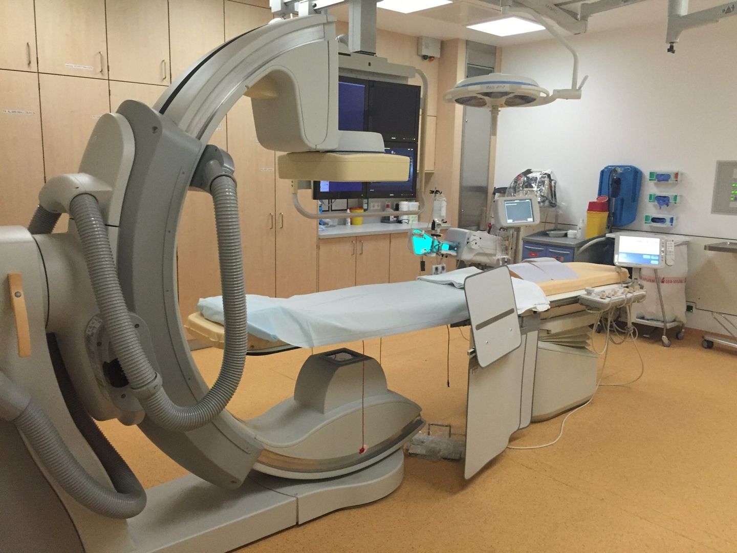 Ein medizinischer Untersuchungsraum mit modernen bildgebenden Geräten, einem Patientenbett mit blauem Bezug und verschiedenen Überwachungsgeräten.